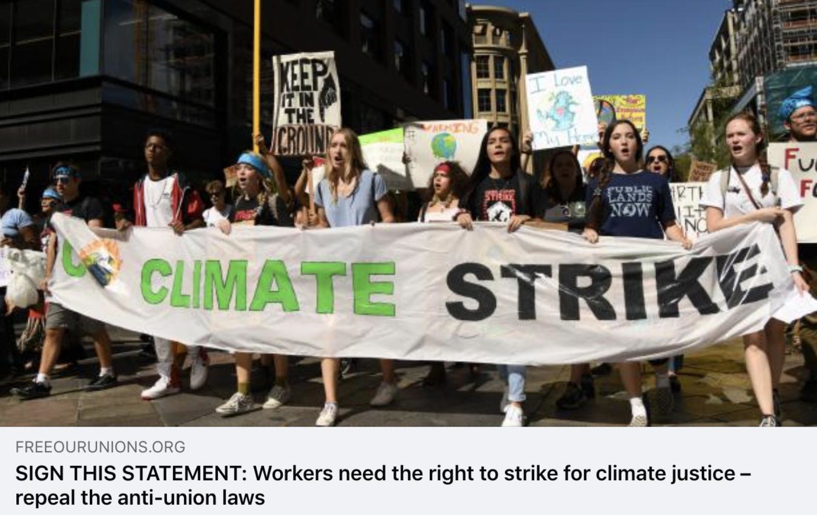 Image shows a groups of people marching and holding a banner which says "Climate Strike"