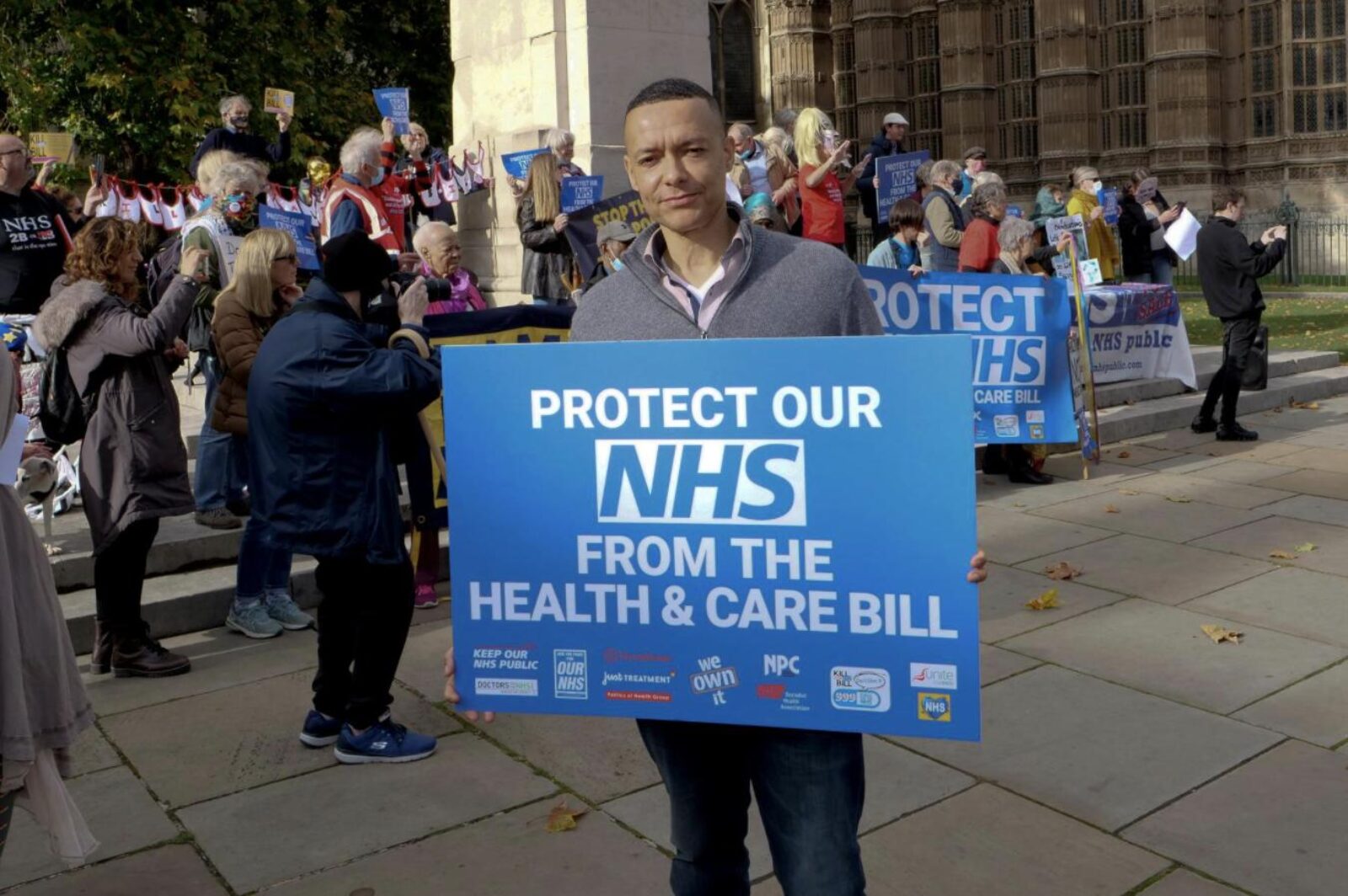 Image shows Clive holding a sign saying 