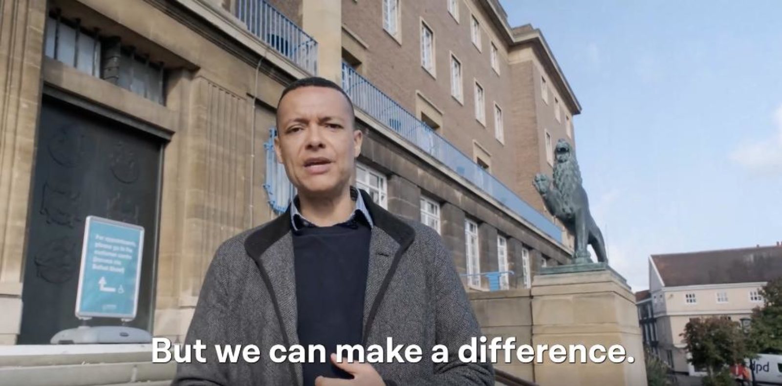 Image shows a still from a video with Clive standing in front of Norwich City Hall. The caption reads 